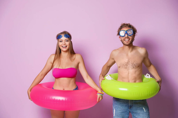 Young couple in beachwear and goggles with inflatable rings on color background - Zdjęcie, obraz