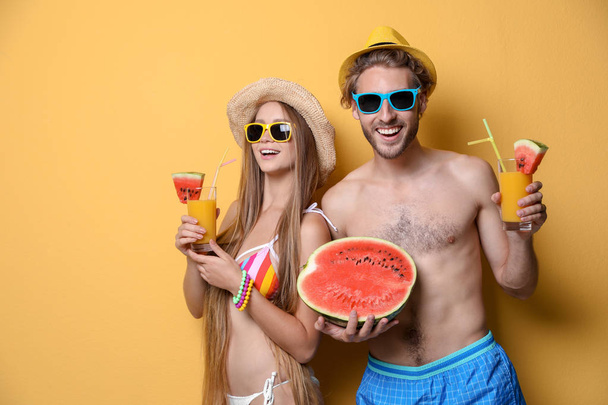 Young couple in beachwear with cocktails on color background - Foto, Imagen