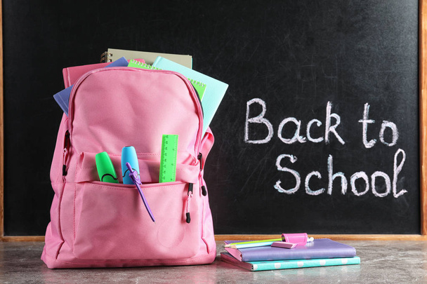 Backpack with stationery on table against blackboard with written words BACK TO SCHOOL - Fotoğraf, Görsel