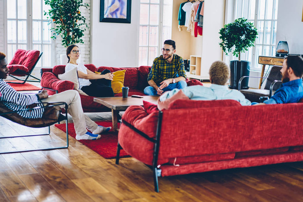 Group of smiling multiracial people resting at modern apartments with comfortable design furniture in house, diversity group of male and female friends talking and having fun on common leisur - Foto, Bild