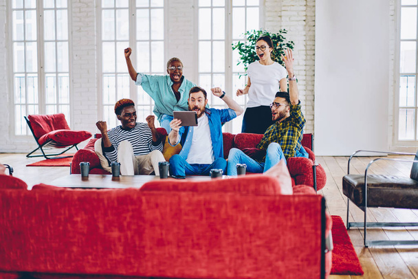 Emotional group of male and female friends cheering for favorite team surprise with  victory watching online on digital tablet, hipsters screaming excited with results of match read on touchpa - Foto, Imagem