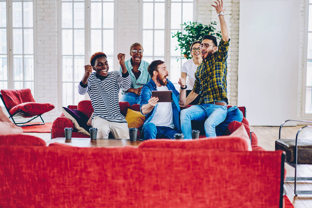 Emotional male and female hipsters expressing happiness cheering for team together watching online match on tablet in loft apartment,group of multiracial friends celebrating victory in competitio - Photo, image