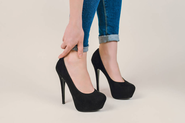 小さすぎるの概念少しスタイリッシュなトレンディな靴をスタイルします。白い背景に分離された黒スエード レザー靴を履いて痛みが足に触れる女性の手の側になってプロフィール写真をクローズ アップ トリミング - 写真・画像