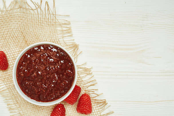 Raspberries jam with fresh red ripe on wooden background with napkin. Top view. - Foto, Bild