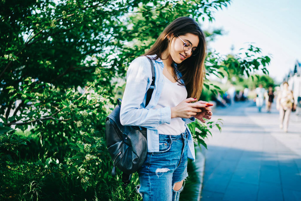 Positive young caucasian woman using mobile phone on street enjoying recreating on spring sunny day, smiling female blogger chatting with followers in social networks via modern cellular outdoors - Fotografie, Obrázek
