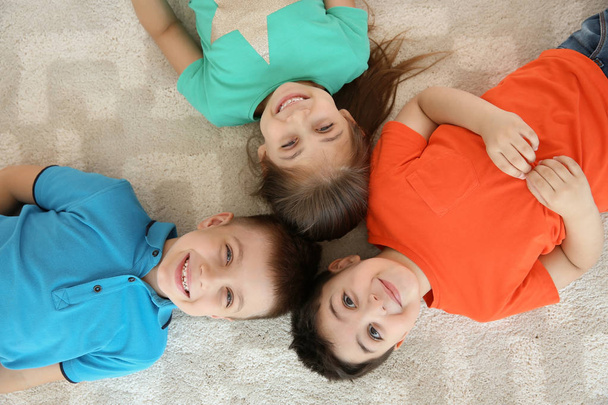 Söpöt pienet lapset makaavat yhdessä lattialla leikkihuoneessa, ylhäältä
 - Valokuva, kuva