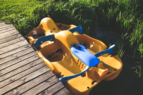 Gelb-blaues Kunststoff-Tretboot in der Nähe des hölzernen Stegs am See. Urlaub, Sommeraktivitäten. - Foto, Bild