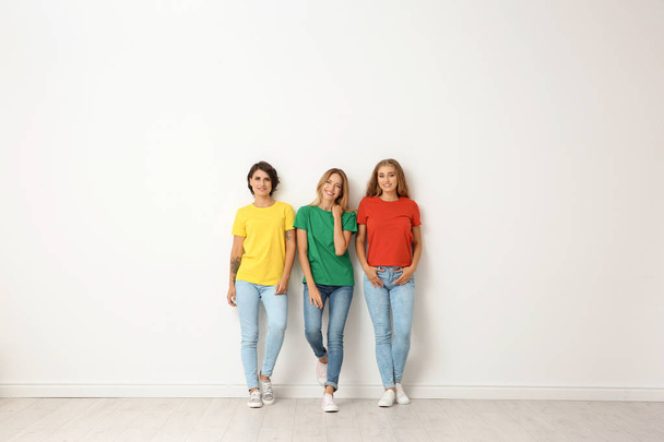 Group of young women in jeans and colorful t-shirts near light wall - Fotoğraf, Görsel