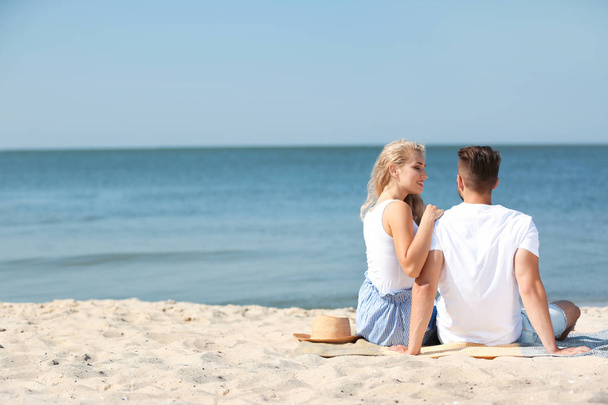 Happy young couple sitting together at beach on sunny day - Foto, Imagem