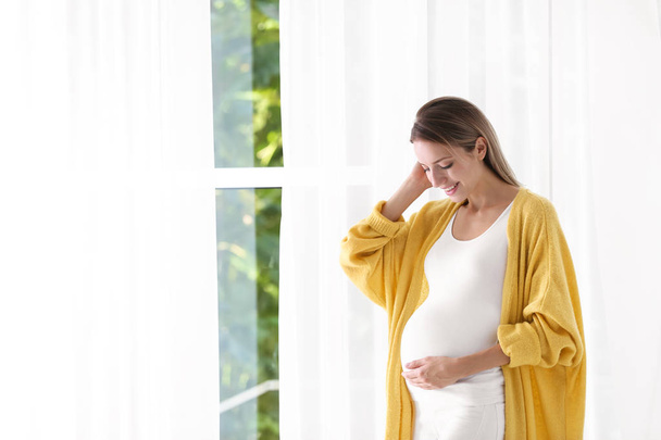 Happy pregnant woman standing near window at home - Foto, Imagen