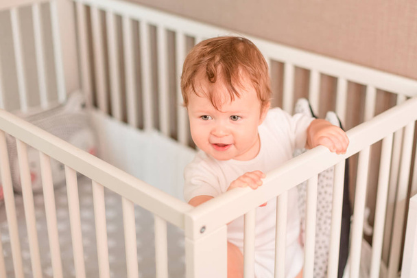 Cute little baby boy looking out of his bed in his room - 写真・画像