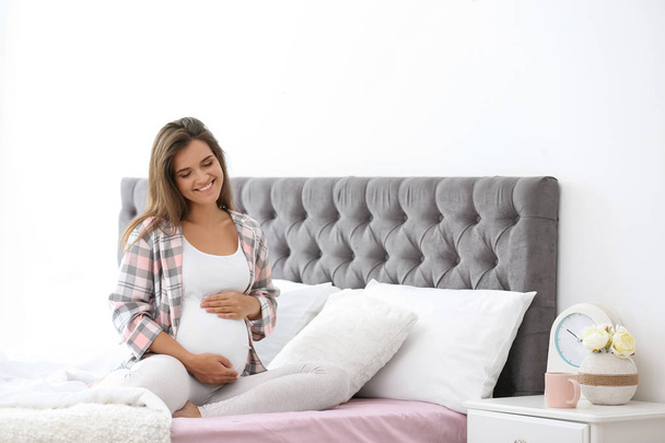 Happy pregnant woman sitting on bed at home - Foto, Imagem
