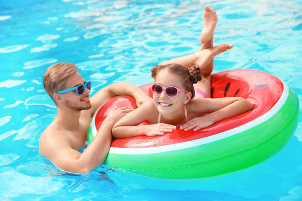 Jonge man met dochter in zwembad op zonnige dag - Foto, afbeelding