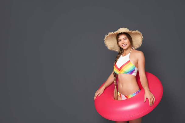 Beautiful young woman in bikini with inflatable ring against dark background. Space for text - Фото, зображення