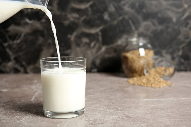 Pouring hemp milk into glass on table, closeup - Φωτογραφία, εικόνα