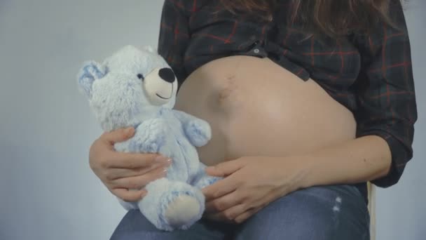 子供の近くで腹演奏テディベアを保持している妊娠中の女性. - 映像、動画