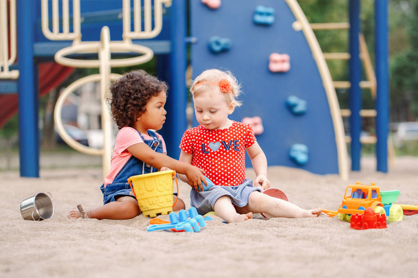 Donne-le-moi. Deux mignons bébés latins blancs et hispaniques assis dans un bac à sable jouant avec des jouets colorés en plastique. Petites filles amis s'amuser ensemble sur l'aire de jeux
. - Photo, image