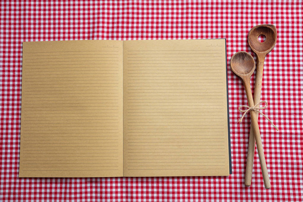 Cooking recipe. Blank notebook and wooden kitchen utensils on red tablecloth, top view, copy space - Photo, Image