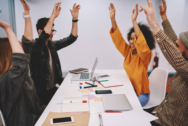 Diverse team of successful students holding hands up celebrating victory of startup project after brainstorming.Group of hipster guys happy with completed educational courses at meeting table - Foto, Bild