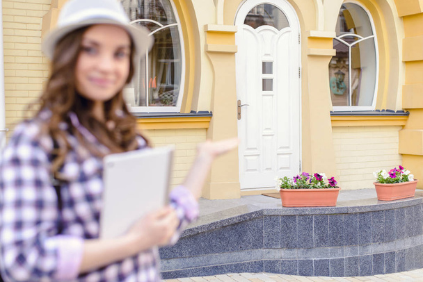 Deal contract people person shop store concept. Close up portrait of pretty professional seller demonstrating gesturing with hand  white door of new yellow house looking in camera holding tablet - Photo, Image