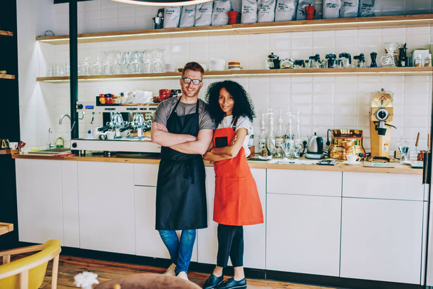 Portrait of multicultural two colleagues baristas in aprons cooperating together on development own business startup.Positive diverse employees of cafeteria with crossed hands smiling at camera - Foto, Imagem