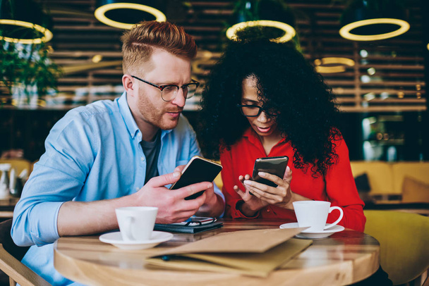 Two multicultural business partners sharing media files on smartphones using bluetooth connection.African american young woman showing caucasian male colleague application on mobile phone device - Fotoğraf, Görsel