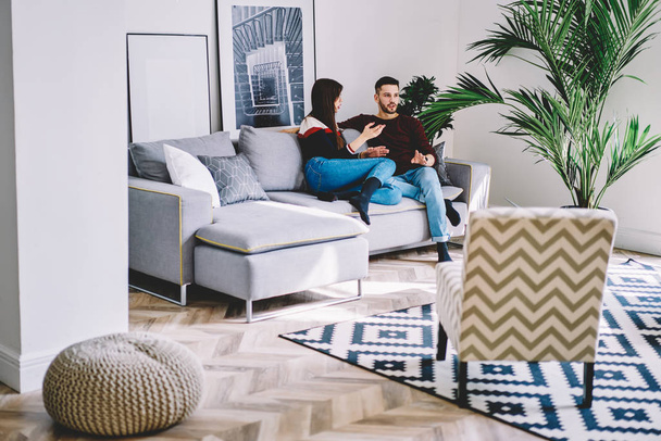 Boyfriend and girlfriend communicating with each other while sitting on comfortable couch and spending leisure time together at home.Young marriage discussing dispute in modern apartment - Fotografie, Obrázek