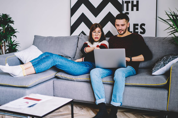 Couple in love watching movie online on website using home internet connection on modern laptop device sitting on comfortable on couch.Young marriage choosing film resting in modern apartment - Fotoğraf, Görsel