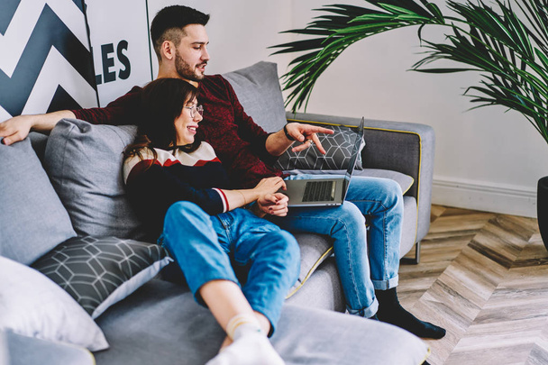 Young marriage discussing choose of movie relaxing together in modern apartment using laptop.Girlfriend and boyfriend updating application on computer spending free time together on sofa at home - 写真・画像