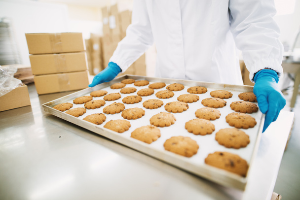 werkneemster houden van vers gebakken koekjes op blikken in voedsel productie fabriek - Foto, afbeelding