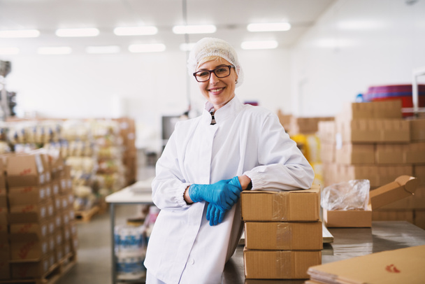Retrato de una trabajadora sonriente con ropa estéril apoyada en paquetes
. - Foto, Imagen