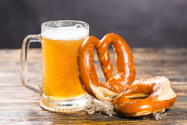 Концепция напитков и продуктов питания - Стакан пива и бублики на деревянном столе
 - Фото, изображение