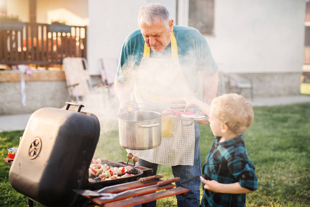 grandfather carefully teaching adorable boy to grill - Foto, Imagen