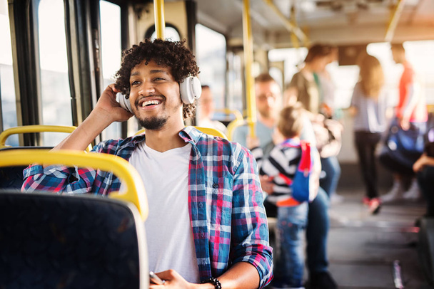 ヘッドセットを介して音楽を聴く、バスの座席に座っている若い幸せな男  - 写真・画像