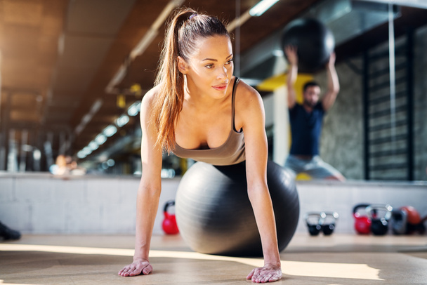 Young beautiful sporty woman doing push ups while lying on a pilates ball - Photo, Image