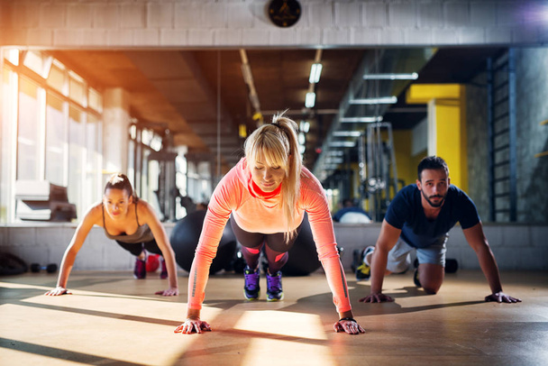 Three focused sporty people preparing them selves for push ups in a gym. - Photo, Image