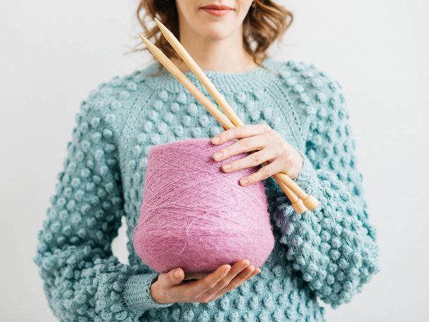 Pretty young woman knits woolen clothes. Girl with knitting needles and wool yarn - Foto, afbeelding