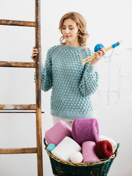 Pretty young woman knits woolen clothes. Girl with knitting needles and wool yarn - Foto, Bild