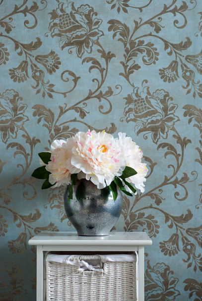 Egy csokor pünkösdi rózsa, az egy fém váza az éjjeliszekrényen a hálószobában. Függőleges fotózás. - Fotó, kép