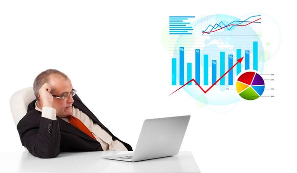 Businessman sitting at desk with laptop and statistics - 写真・画像