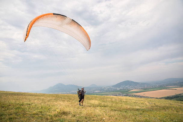 The paraglider opens his parachute before taking off from the mountain in the North Caucasus. Filling the parachute wing with air before takeoff - Фото, изображение