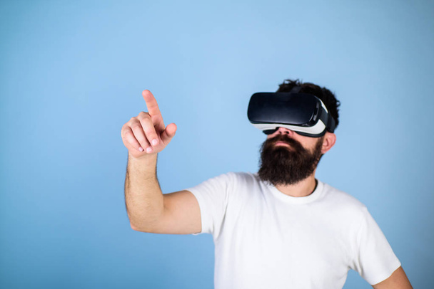 Man with beard in VR glasses, light blue background. Interactive surface concept. Guy with head mounted display interact in virtual reality. Hipster on busy face exploring virtual reality with gadget - Photo, Image