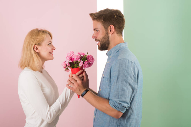Man congratulates woman birthday anniversary holiday, pastel background. Gift concept. Man gives bouquet flowers to girlfriend. Couple in love celebrating holiday. Couple date bouquet flowers gift - 写真・画像