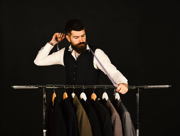Tailor with serious face holds measuring tape near custom jackets - Fotoğraf, Görsel