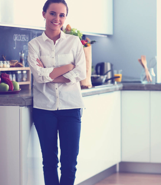 Portrait of young woman standing with arms crossed against kitchen background - Foto, immagini