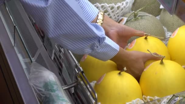 Frau wählt Melone, die im Supermarkt ins Regal gestellt wird. - Filmmaterial, Video
