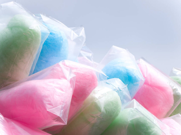 Borse colorate piene di zucchero filato tra cui verde, rosa, blu e viola su un bastone venditore ambulante durante un evento con cielo grigio oltre
. - Foto, immagini