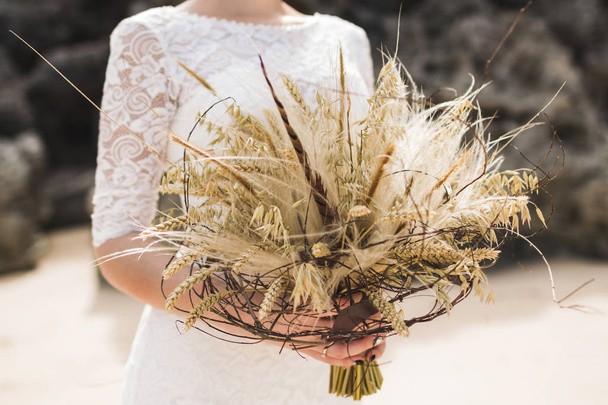 Свадебный букет с сушеными цветами и шипами в стиле Бохо в руках невесты
 - Фото, изображение