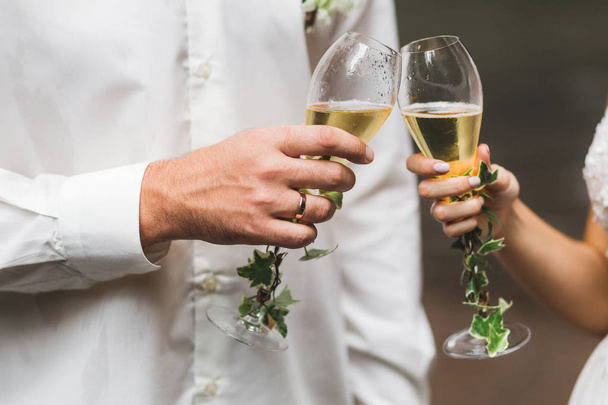 Manos de hombre y mujer sosteniendo dos copas de champán decoradas con flores para la ceremonia de boda
 - Foto, Imagen