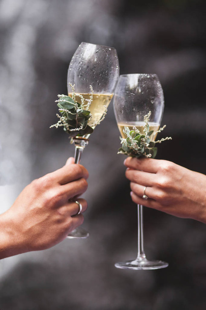 Man and woman hands holding two champagne glasses decorated with flowers for wedding ceremony - Foto, Imagem